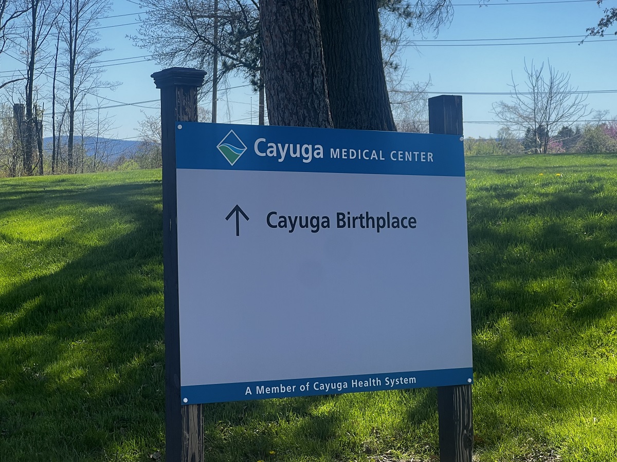 Sign for Cayuga Medical Center with an arrow pointing up labeled 'Cayuga Birthplace' on a grassy lawn
