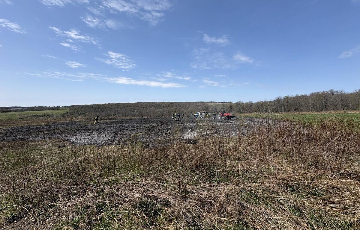 Group of people in safety vests near trucks in a muddy field on a clear day.