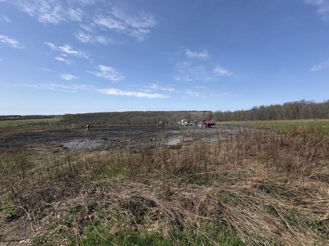 Group of people in safety vests near trucks in a muddy field on a clear day.