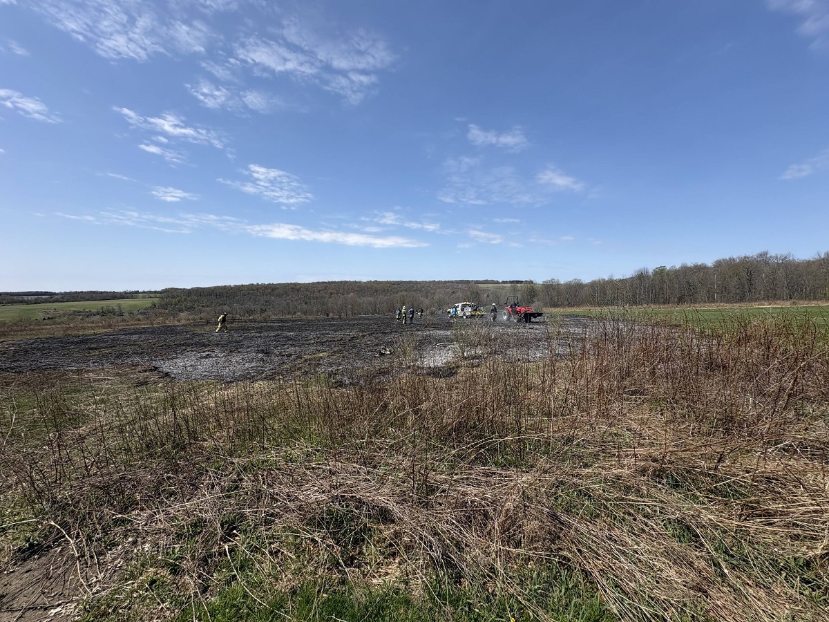 Group of people in safety vests near trucks in a muddy field on a clear day.