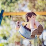 Child on a swing flying through the air on a sunny outdoor playground.
