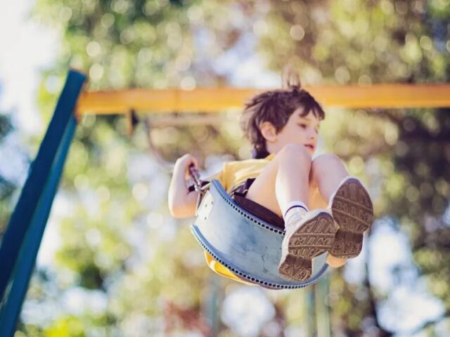 Child on a swing flying through the air on a sunny outdoor playground.