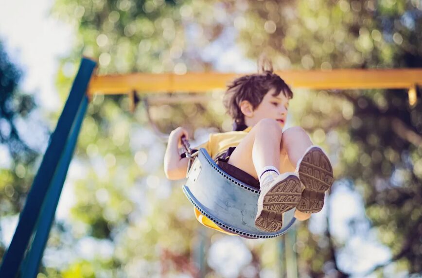 Child on a swing flying through the air on a sunny outdoor playground.