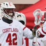 Lacrosse players in Cortland white jerseys high-fiving on the field, #42 visible on the front.