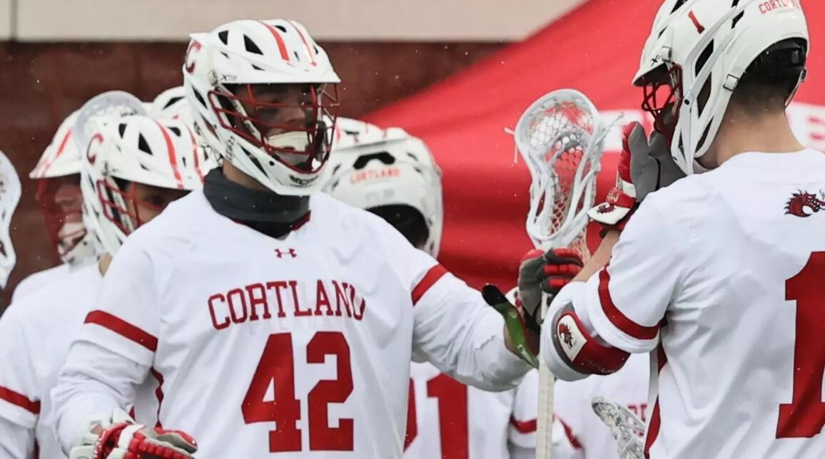 Lacrosse players in Cortland white jerseys high-fiving on the field, #42 visible on the front.