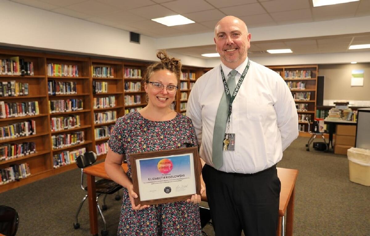 Elizabeth Kozlowski holds a framed certificate of achievement with a smiling man in a library.