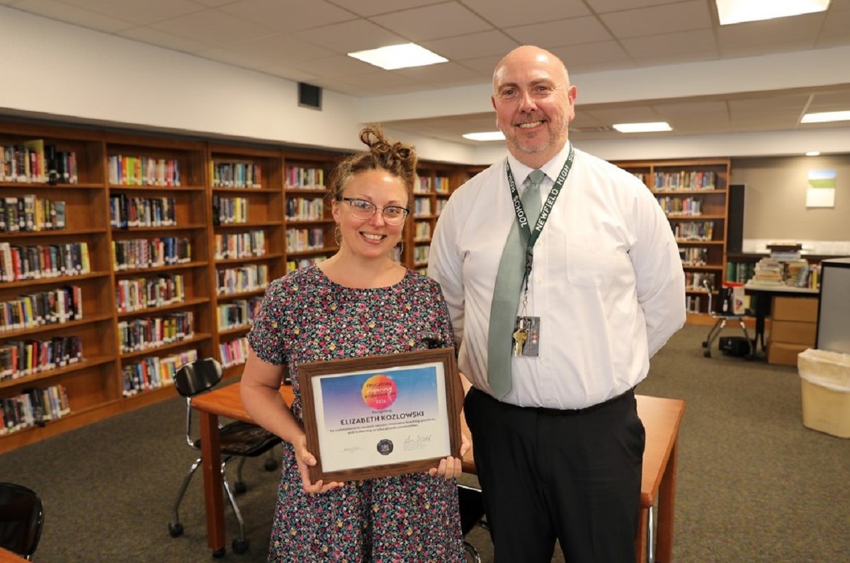 Elizabeth Kozlowski holds a framed certificate of achievement with a smiling man in a library.