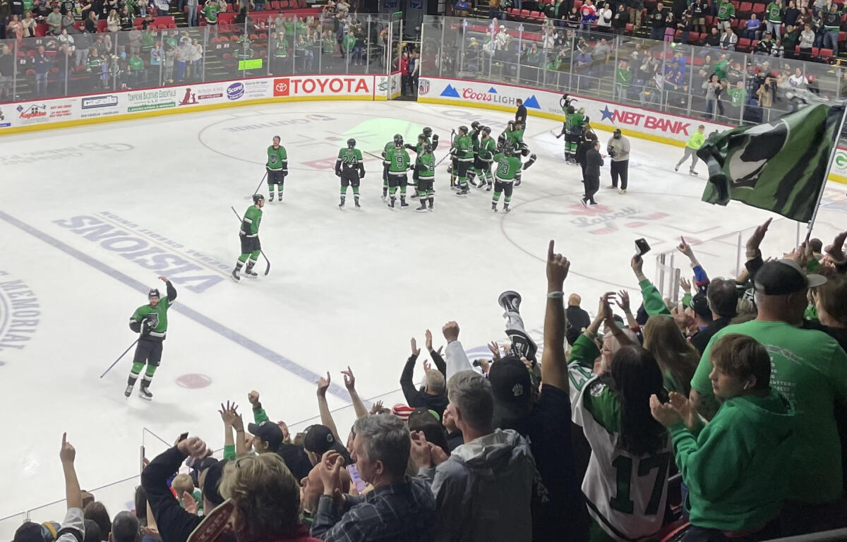 Green-uniform hockey players celebrate on the ice as a cheering crowd watches from the stands.