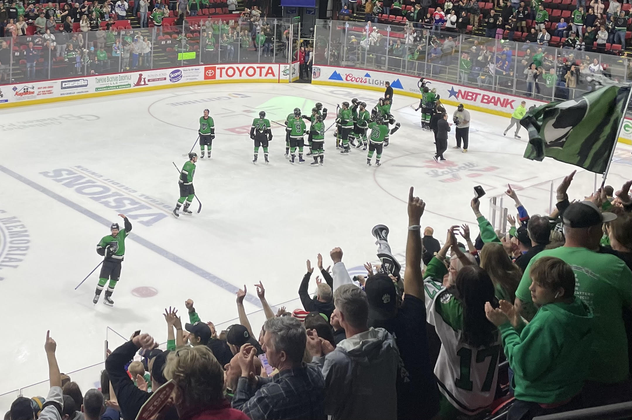 Green-uniform hockey players celebrate on the ice as a cheering crowd watches from the stands.