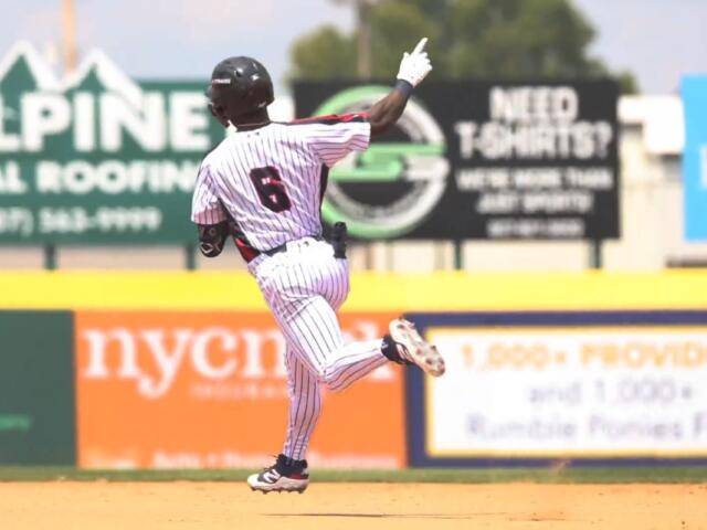 Back view of a baseball player in a white pinstriped uniform running on the dirt infield, number 6 visible on jersey, during a game.