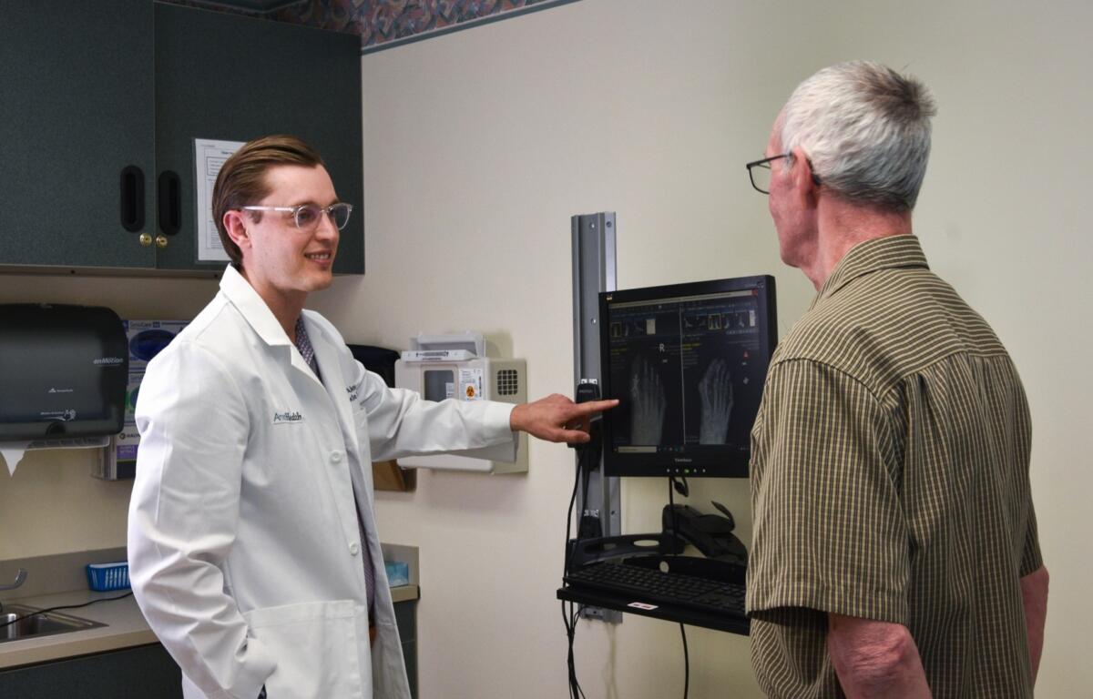 Doctor in white coat shows and explains X-ray images to an older man in a clinic setting.