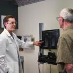 Doctor in white coat shows and explains X-ray images to an older man in a clinic setting.