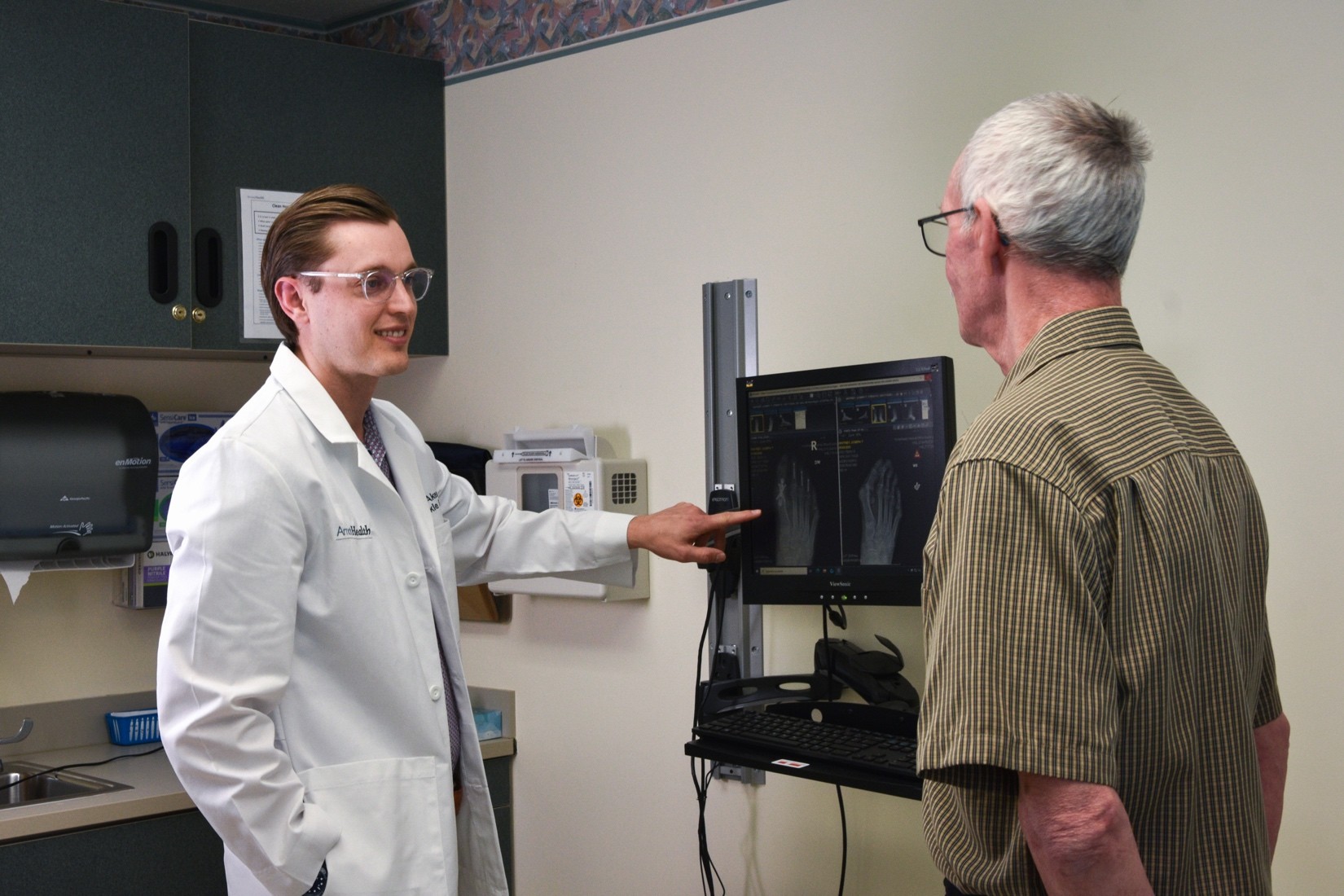 Doctor in white coat shows and explains X-ray images to an older man in a clinic setting.