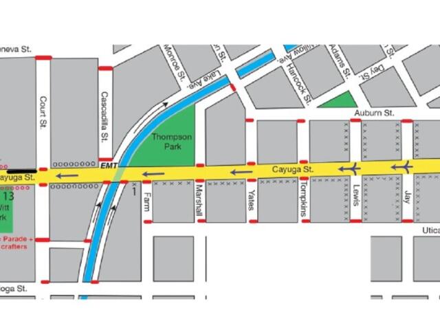 Map showing a parade route through a downtown area: yellow street (Cayuga St) as main path, red dashed lines indicate barriers, green parks (T13 DeWitt Park, Thompson Park), blue canal/stream, and surrounding streets labeled (Geneva St, Buffalo St, Tioga St, Utica St).
