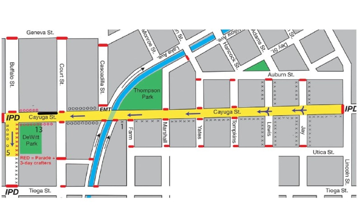 Map showing a parade route through a downtown area: yellow street (Cayuga St) as main path, red dashed lines indicate barriers, green parks (T13 DeWitt Park, Thompson Park), blue canal/stream, and surrounding streets labeled (Geneva St, Buffalo St, Tioga St, Utica St).