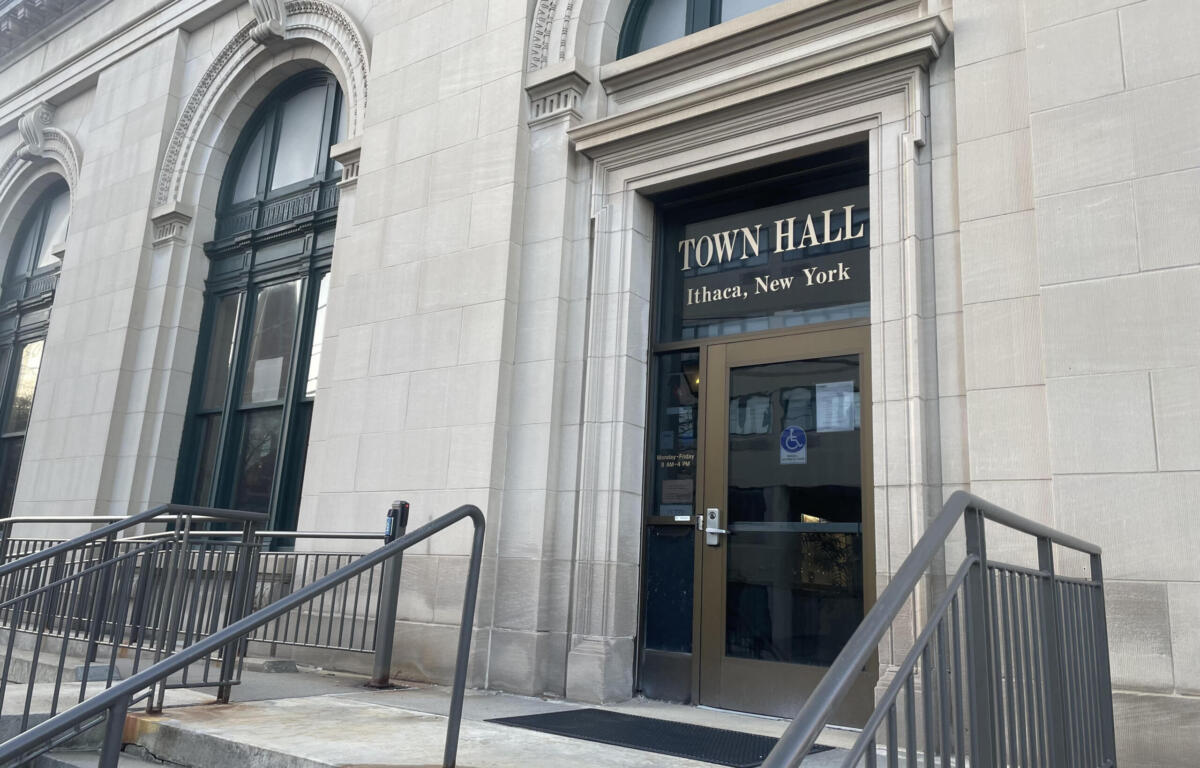 Front of Town Hall Ithaca, New York, showing a stone facade, arched windows, and a glass door with beige frame behind metal railings.