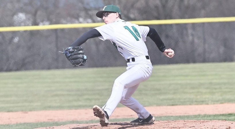 Baseball pitcher in a white uniform and green cap delivering a pitch from the mound, with glove arm extended forward.