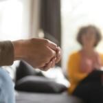 Close-up of two people holding hands during a counseling session in a living room setting.