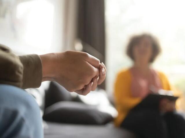 Close-up of two people holding hands during a counseling session in a living room setting.