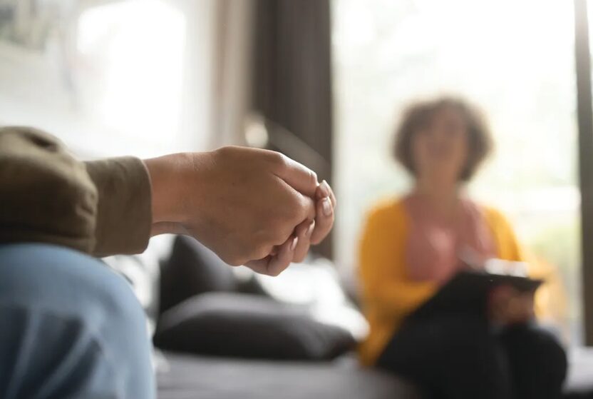 Close-up of two people holding hands during a counseling session in a living room setting.