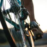 Close-up of a cyclist's foot on a pedal and bicycle chain, with warm sunset light in the background (motion shot).