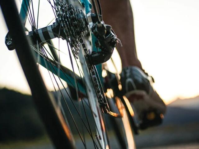 Close-up of a cyclist's foot on a pedal and bicycle chain, with warm sunset light in the background (motion shot).