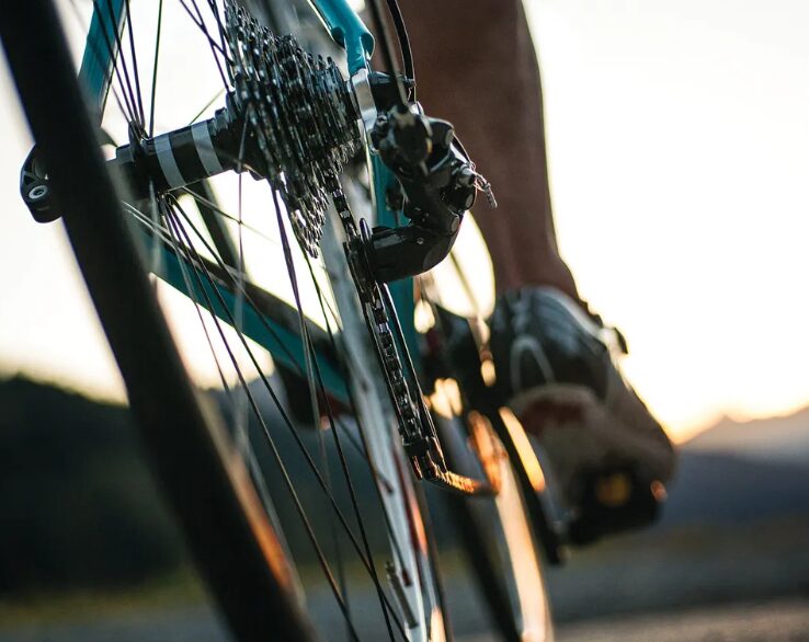 Close-up of a cyclist's foot on a pedal and bicycle chain, with warm sunset light in the background (motion shot).