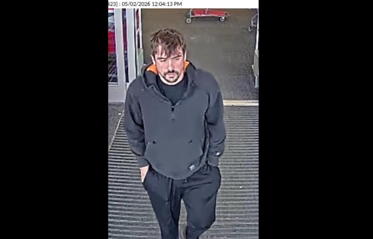 Surveillance image of a man in a dark hoodie and black joggers walking toward the camera at a store entrance, hands in pockets; timestamp shows 05/02/2026 12:04:13 PM.