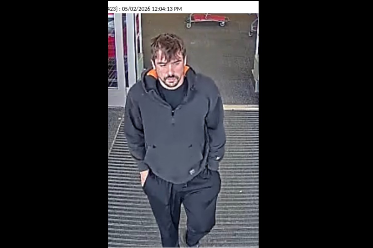 Surveillance image of a man in a dark hoodie and black joggers walking toward the camera at a store entrance, hands in pockets; timestamp shows 05/02/2026 12:04:13 PM.
