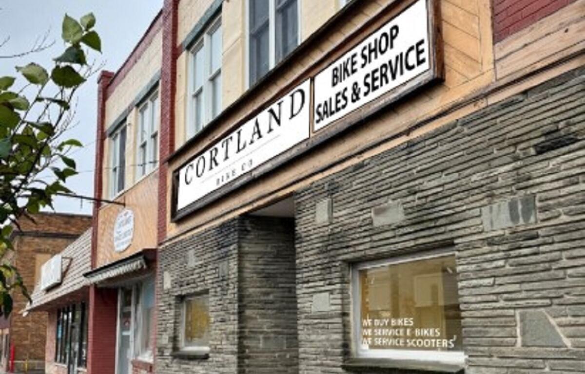 Cortland Bike Shop storefront with a large white sign reading 'CORTLAND BIKE SHOP SALES & SERVICE' over a stone facade.