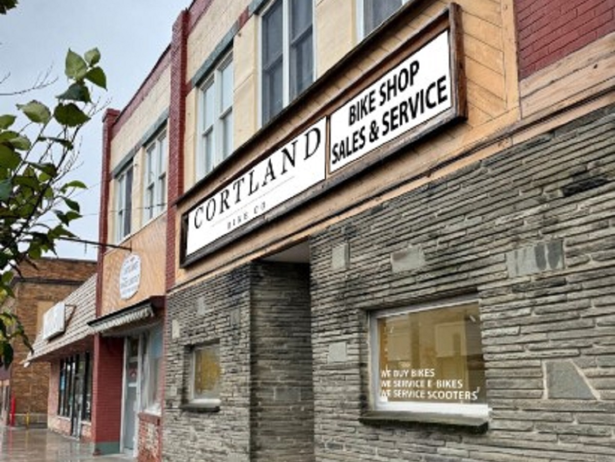 Cortland Bike Shop storefront with a large white sign reading 'CORTLAND BIKE SHOP SALES & SERVICE' over a stone facade.