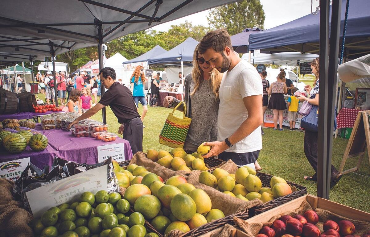 Couple browsing fresh fruit at an outdoor farmers market under tents on a sunny day.