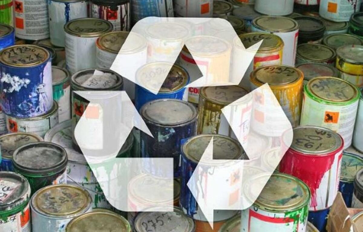Paint cans piled together with a large translucent recycling symbol overlaid, signaling paint recycling.