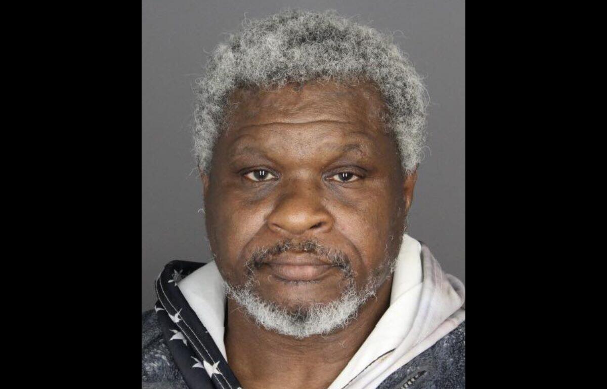 Mugshot photo of an African American man with gray hair and beard, wearing a dark jacket over a light hoodie, neutral expression against a gray backdrop.