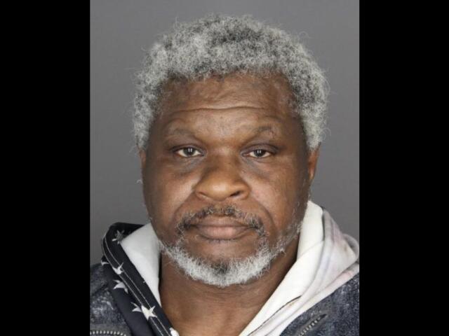 Mugshot photo of an African American man with gray hair and beard, wearing a dark jacket over a light hoodie, neutral expression against a gray backdrop.