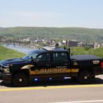Chemung County Sheriff pickup truck parked on a road, with a river, city buildings, and forested hills in the background.