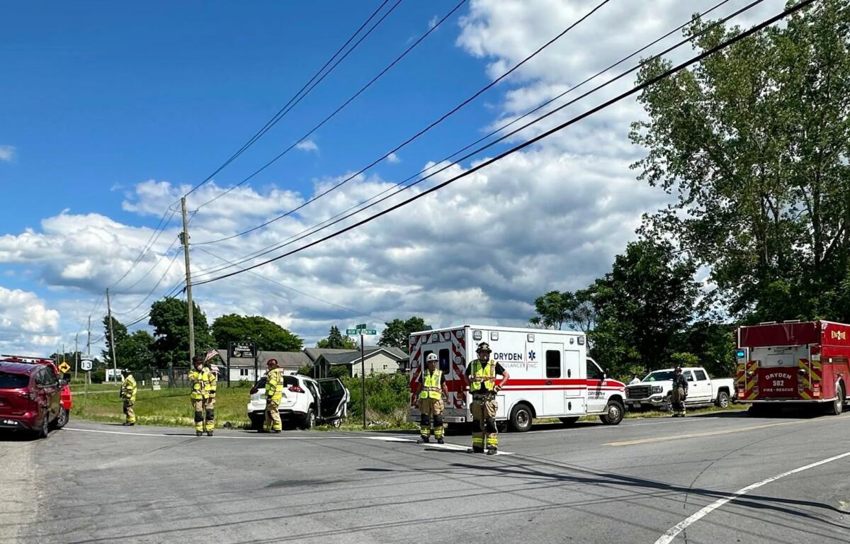 Emergency responders and a white ambulance on a street, with firefighters and fire trucks at the scene under power lines.