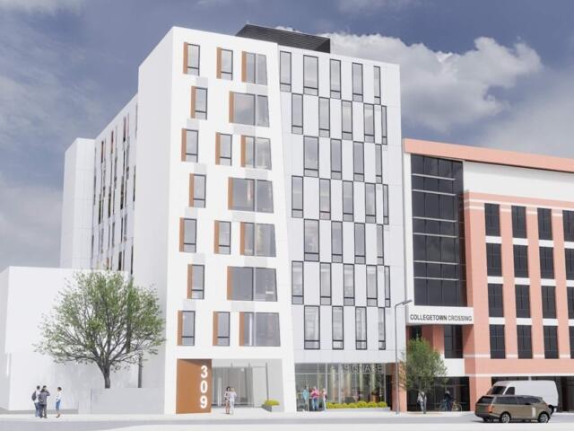 Contemporary mixed-use building with white and brick facades, tall windows, and pedestrians on the sidewalk under a blue sky; Collegetown Crossing sign visible.