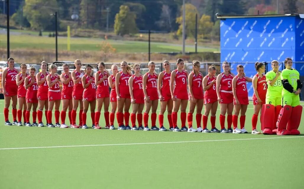 Girls' soccer team in red uniforms lined up on a field, with two neon yellow goalkeepers on the right side.