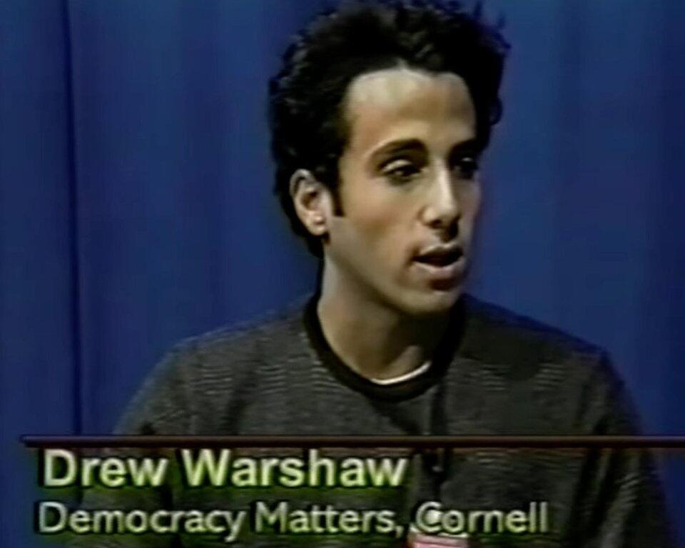 Young man speaking in a TV interview; on-screen text reads 'Democracy Matters, Cornell' (no identifying name shown).