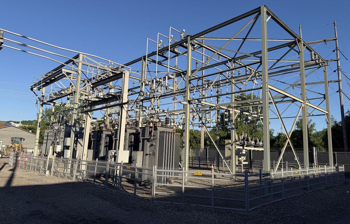 High-voltage electrical substation with metal framework, transformers, and fencing under a clear blue sky