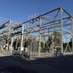 High-voltage electrical substation with metal framework, transformers, and fencing under a clear blue sky