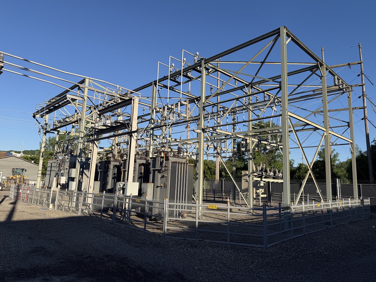 High-voltage electrical substation with metal framework, transformers, and fencing under a clear blue sky