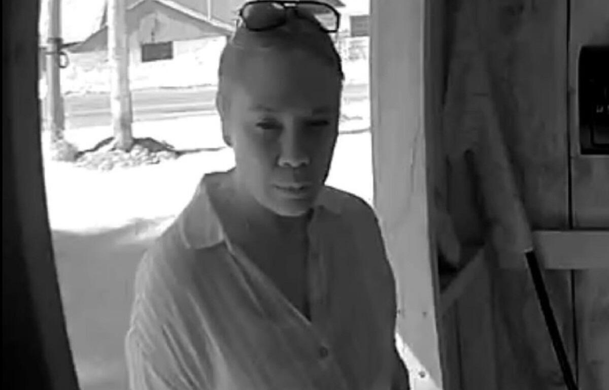 Woman in a light shirt stands at a doorway, sunglasses on her head, looking toward the camera.