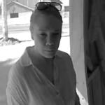 Woman in a light shirt stands at a doorway, sunglasses on her head, looking toward the camera.