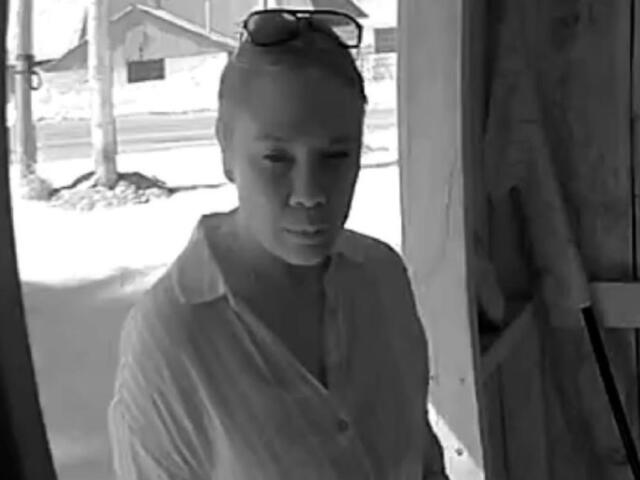 Woman in a light shirt stands at a doorway, sunglasses on her head, looking toward the camera.