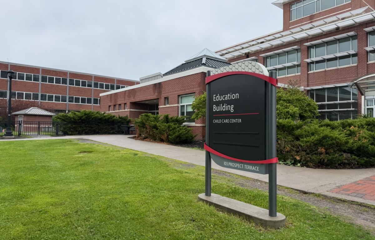 Campus sign reads 'Education Building' with 'Child Care Center' below, located at 103 Prospect Terrace, in front of brick campus buildings and green landscaping.