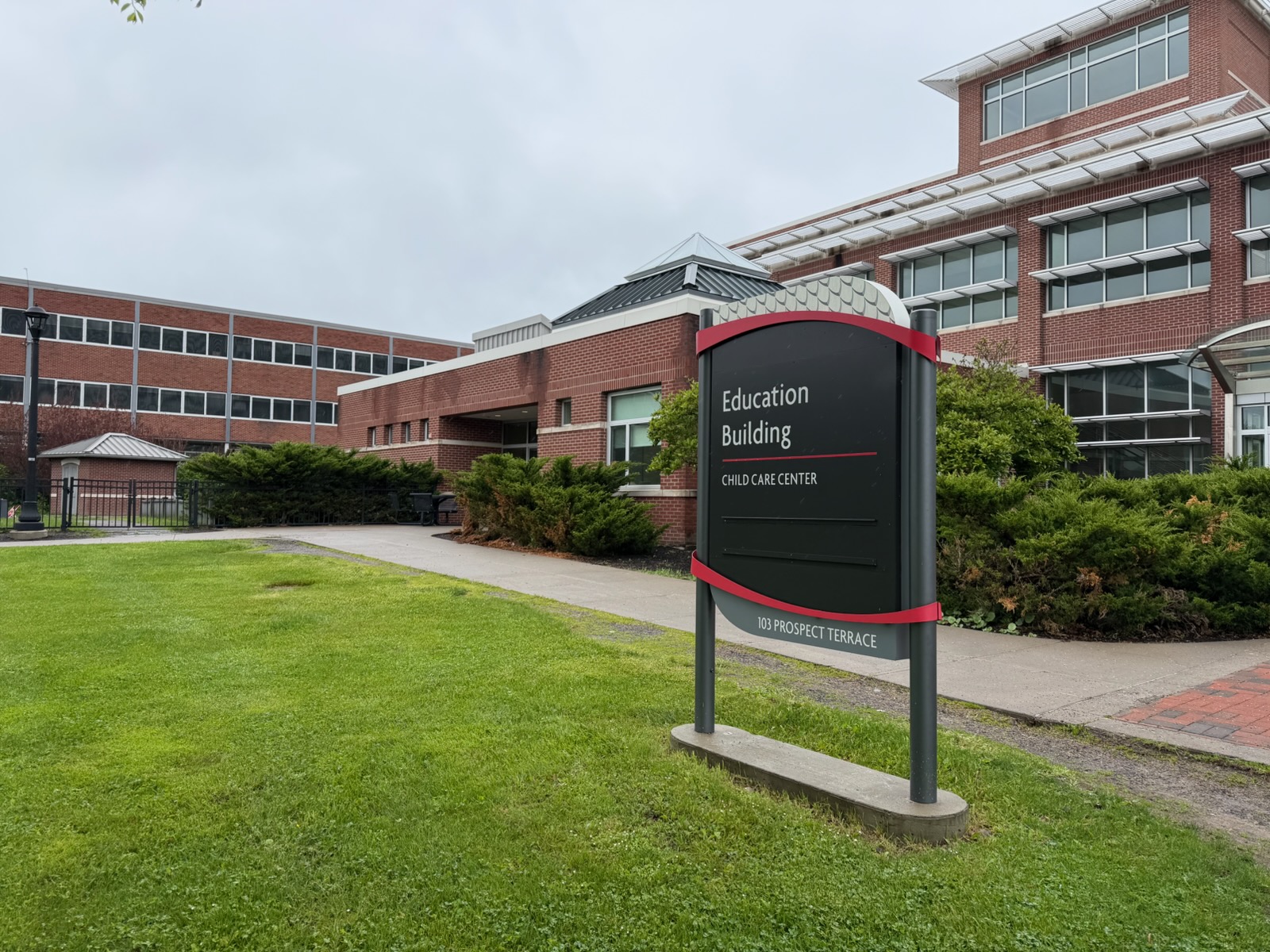 Campus sign reads 'Education Building' with 'Child Care Center' below, located at 103 Prospect Terrace, in front of brick campus buildings and green landscaping.