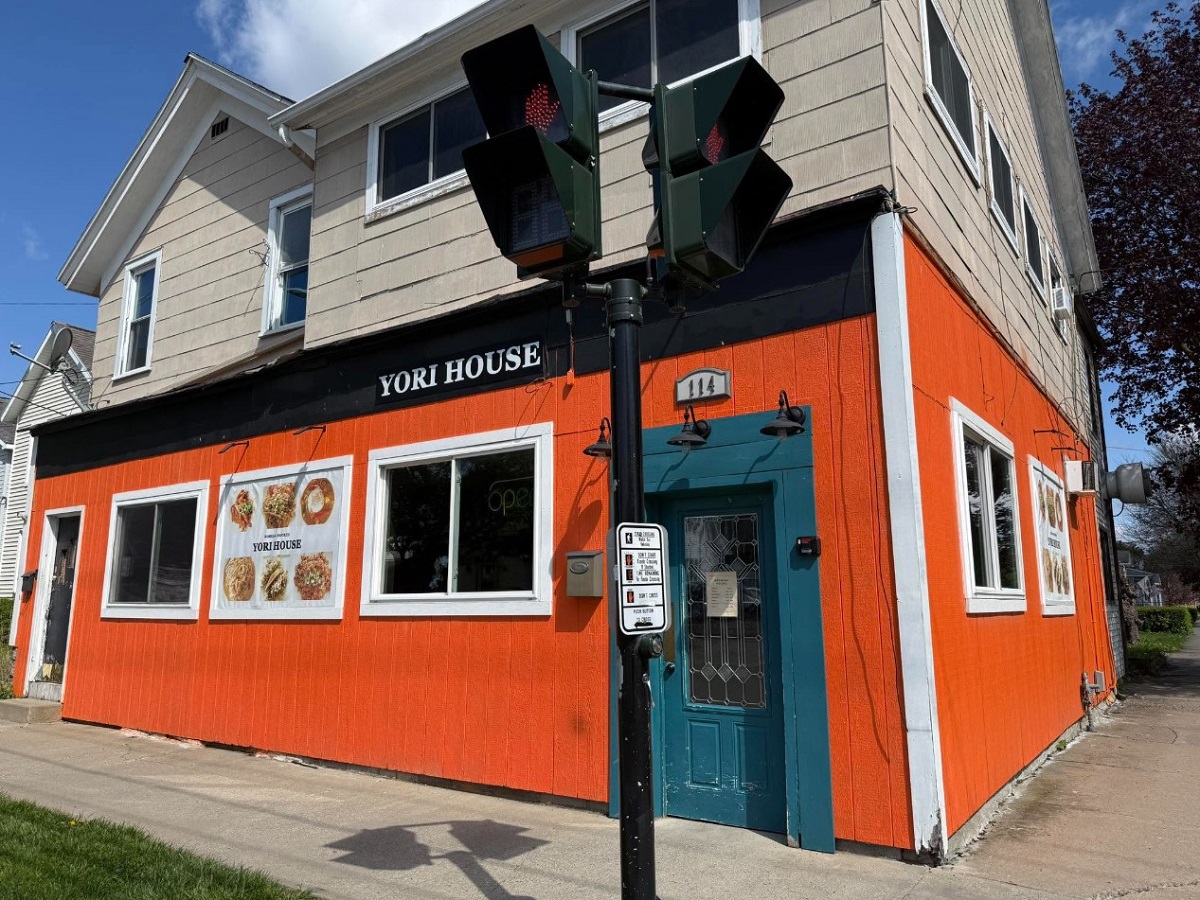 Front view of Yori House restaurant, a bright orange building with a teal door and menu posters in the windows, on a sunny day.