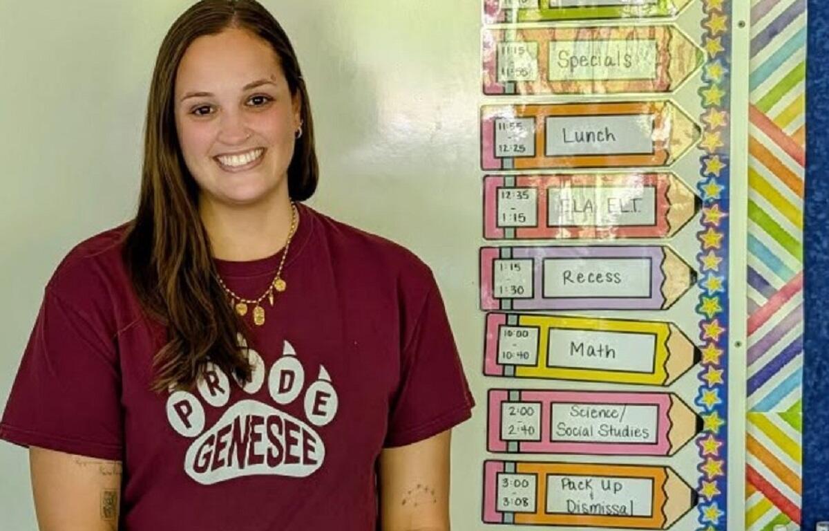 Smiling female student in a maroon shirt standing next to a colorful classroom schedule display showing periods like Lunch and Math.
